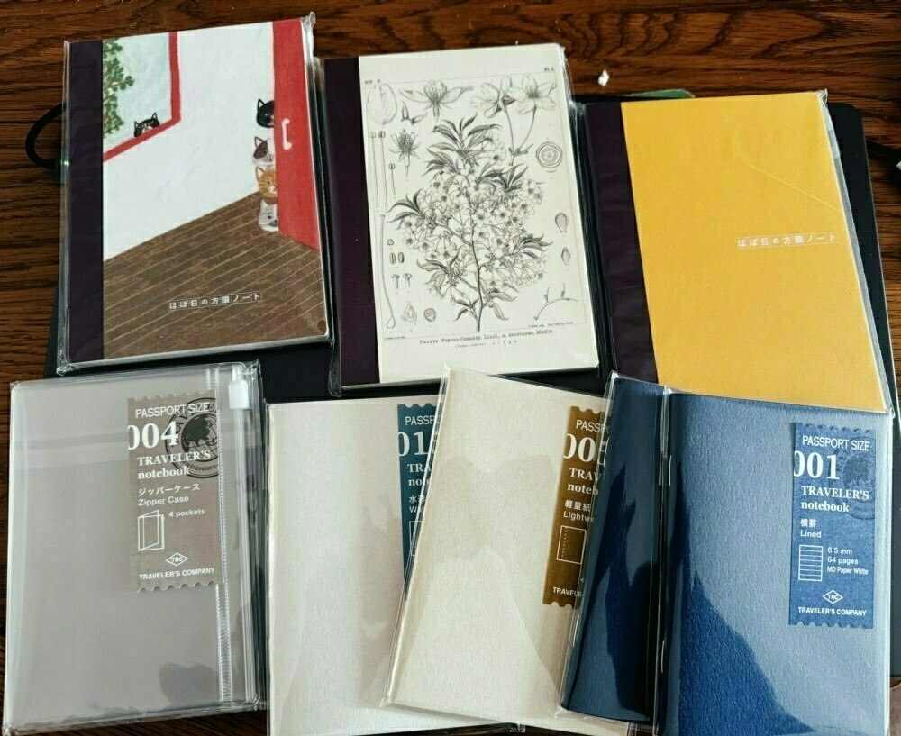 A
collection of notebooks and journals, some with unique covers and 
others labeled by their types and sizes, are displayed on a wooden 
surface.